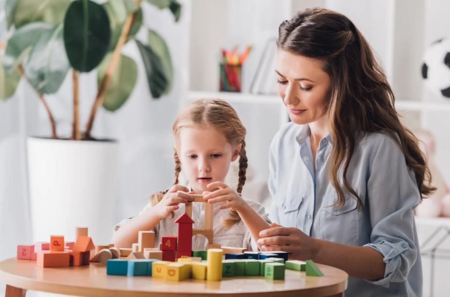 Mother and daughter build with colorful wooden blocks at a round table in a bright, cozy room.